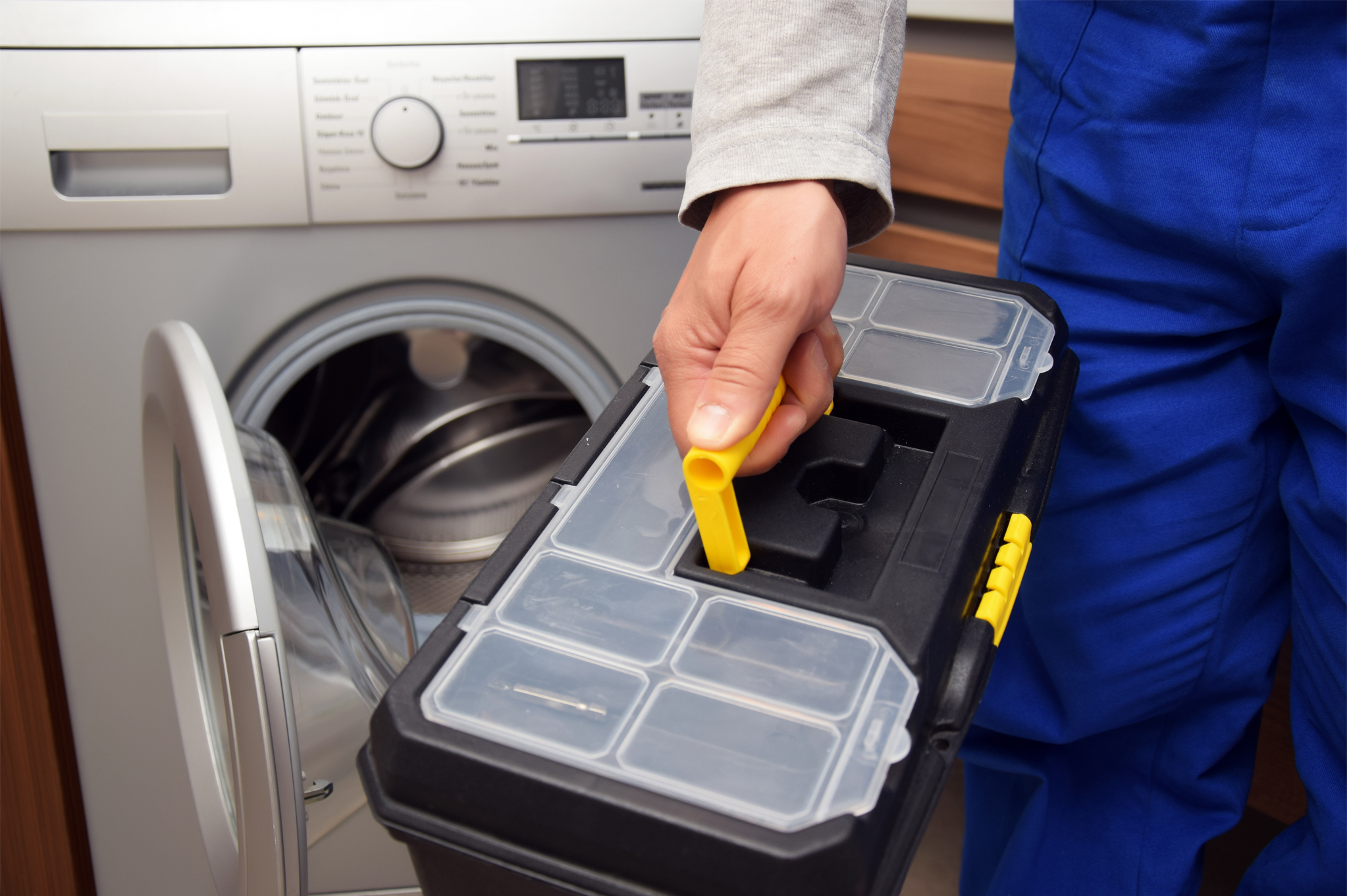 Appliance repair technician holding toolbox in front of washing machine